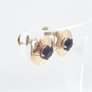 May include: A pair of gold tone earrings with a flower design and dark red gemstones.