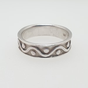 May include: A silver band ring with a wavy design and small circles around the band.