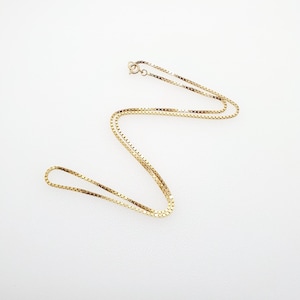 May include: A gold chain necklace with a box chain style. The chain is made of small, square links.