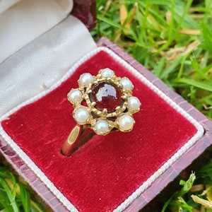 Op de afbeelding: Een gouden ring met een rode edelsteen omringd door witte parels.