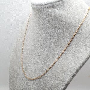 May include: A gold chain necklace on a gray fabric background.