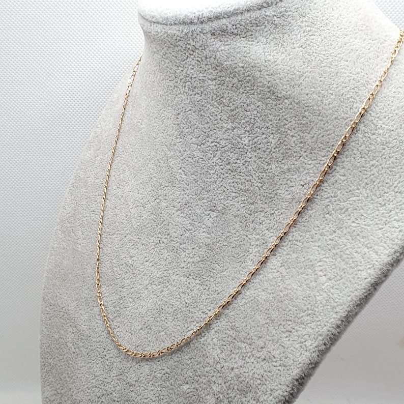 May include: A gold chain necklace on a gray fabric background.