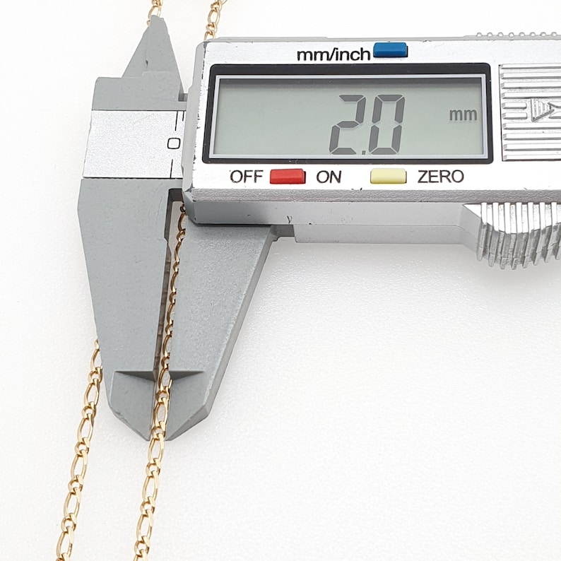 May include: A close-up of a gold chain being measured with a digital caliper. The caliper reads 2.0 mm.