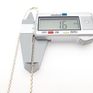 May include: A gold-colored chain necklace is measured with a digital caliper. The digital display reads 1.6 mm. The caliper is silver with black text and red and blue accents. The chain is thin and delicate.