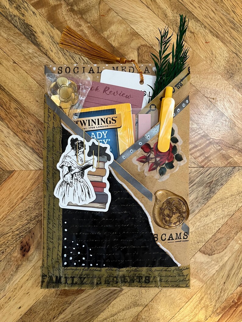 K&ouml;nnte beinhalten: Ein handgefertigtes Journal mit einem Collage-Design. Das Journal enth&auml;lt eine goldene Quaste, einen Aufkleber einer lesenden Frau und einen Teebeutel. Die W&ouml;rter "SOCIAL MEDIA" und "BOOK REVIEW" sind sichtbar.