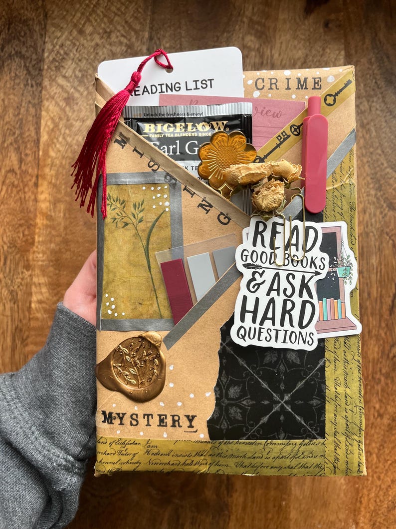K&ouml;nnte beinhalten: Dekorative Geschenkverpackung mit den W&ouml;rtern "Mystery" und "Crime". Enth&auml;lt einen Teebeutel, einen Lesezeichen mit "Reading List" und einen Aufkleber mit "Read Good Books & Ask Hard Questions". Mit roter Quaste.