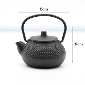 Pode incluir: Bule de ferro fundido preto com superfície texturizada e alça. A chaleira tem 8 cm de altura e 8 cm de largura.