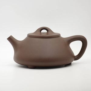 Peut inclure: Une théière en céramique brune avec un corps arrondi et un couvercle avec un petit bouton. La théière a un bec verseur et une poignée.