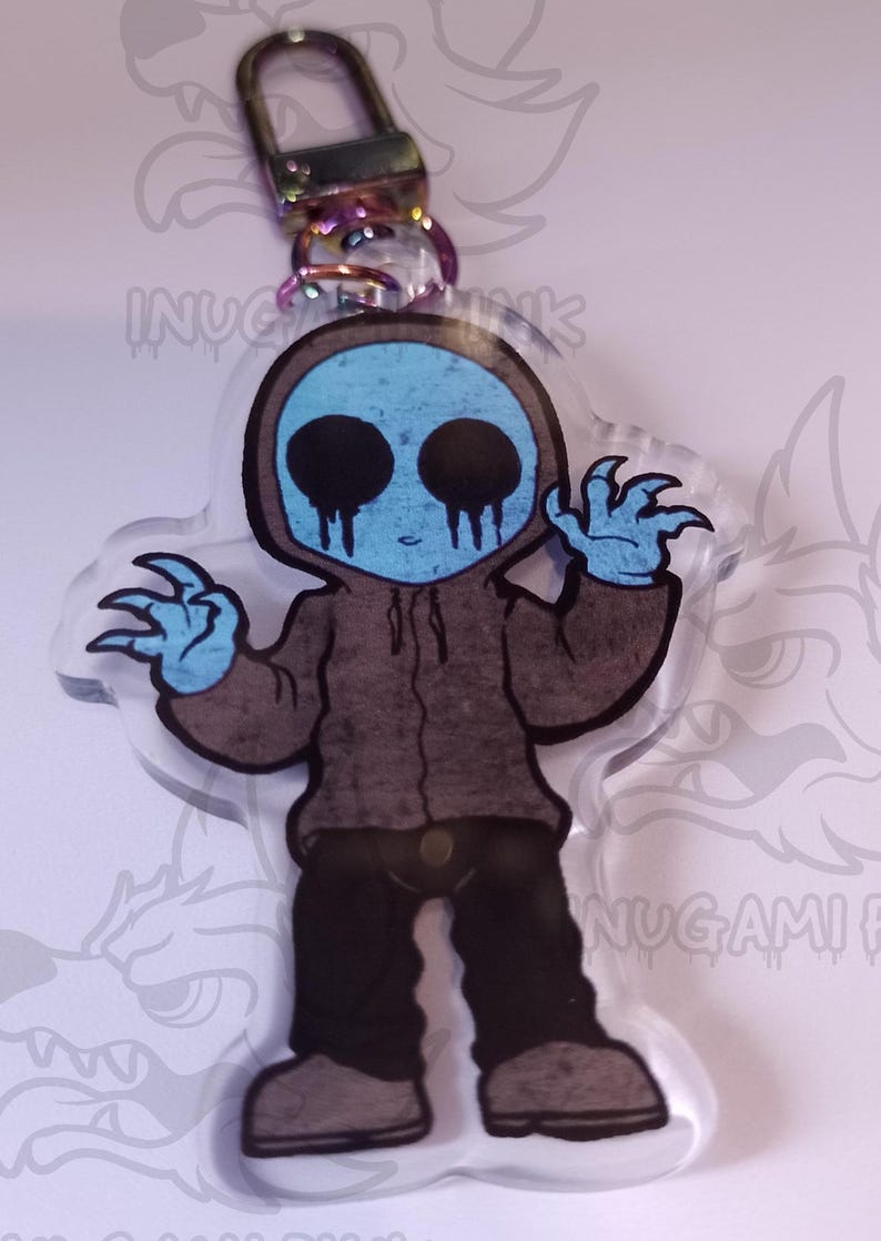 May include: A blue and brown cartoon character with black eyes and a black hooded sweatshirt. The character has a creepy smile and is holding out its hands with claws. The character is on a clear acrylic keychain.