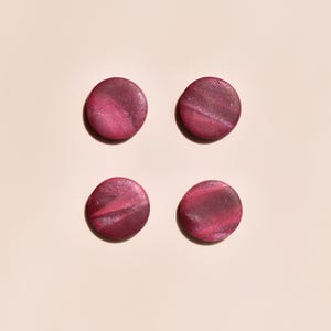 May include: Four round, flat, dark pink objects with a shimmering, marbled effect are arranged in a square on a light beige background. The objects have a slightly irregular shape and appear to be made of a solid material.