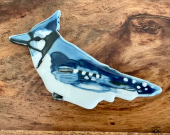Könnte beinhalten: Eine blaue und weiße Keramik-Vogelfigur in Form eines Blauhähers. Der Vogel hat ein detailliertes Design mit schwarzen Akzenten und weißen Punkten.