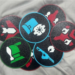 May include: Set of eight round black and white coasters with various graphic designs. The designs include a spaceship, a bomb, a gun, a helmet, and a robot. The coasters are made of a textured material.