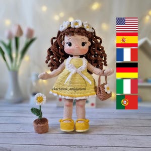May include: A handmade crochet doll with brown curly hair, wearing a yellow dress, shoes, and a flower crown. The doll holds a small brown purse with a flower. A crochet flower in a pot is also present.