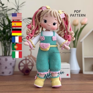 May include: A handmade crochet doll with blonde hair styled in pigtails, wearing a teal jumpsuit with pink accents and yellow boots. The doll has a sweet expression and is holding a small pink purse. The text "PDF PATTERN" is visible.