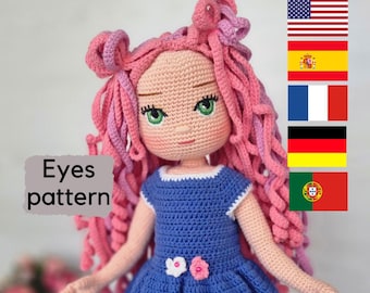 Puede incluir: Muñeca de crochet con pelo rosa, vestido azul y ojos verdes. La muñeca lleva un vestido azul con ribetes blancos y un adorno de flor rosa. Los ojos de la muñeca son verdes y tienen pupilas negras. El pelo de la muñeca es rosa y rizado. La muñeca está de pie sobre un fondo blanco. El texto "Eyes pattern" es visible en la imagen.