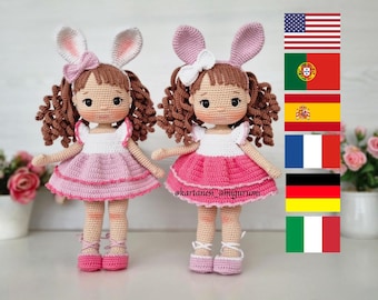May include: Two crocheted dolls with pink dresses and bunny ears. The dolls have brown curly hair and are wearing pink shoes. The dolls are standing on a white surface. The image also includes flags of the United States, Portugal, Spain, France, Germany, and Italy.