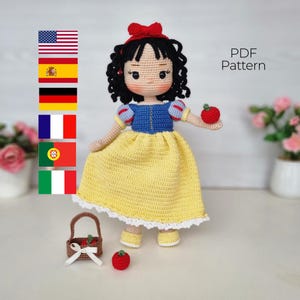 Puede incluir: Muñeca de ganchillo hecha a mano que se asemeja a Blancanieves, con una parte superior azul, un vestido amarillo y un lazo rojo. La muñeca sostiene una manzana roja y está acompañada de una pequeña cesta y otra manzana. El texto "PDF Pattern" es visible.