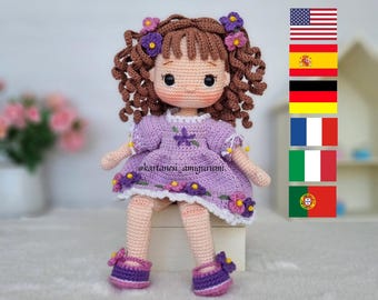 Könnte beinhalten: Handgefertigte Häkelpuppe mit braunen Locken, die ein lila Kleid mit Blumendetails trägt. Die Puppe hat einen süßen Ausdruck und trägt passende lila Schuhe. Der Text "@kartanesi_amigurumi" ist sichtbar.