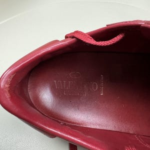May include: Close-up of the inside of a red leather shoe with the brand name "VALENTINO" and "MADE IN ITALY" printed on the insole.