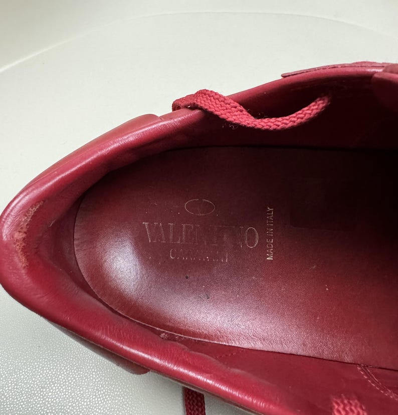 May include: Close-up of the inside of a red leather shoe with the brand name "VALENTINO" and "MADE IN ITALY" printed on the insole.