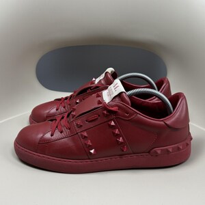 May include: A pair of red leather trainers with a studded design. The trainers have a white label on the side with the text "II" and "Made in Italy".