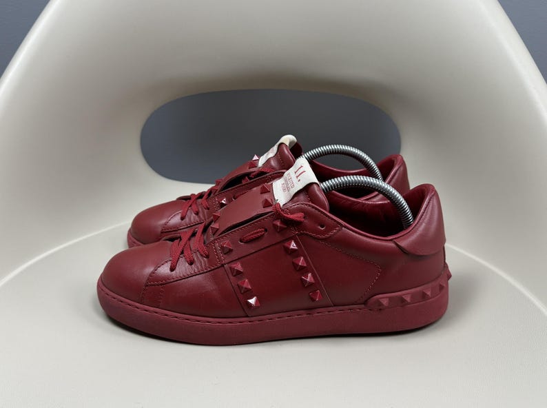 May include: A pair of red leather trainers with a studded design. The trainers have a white label on the side with the text "II" and "Made in Italy".