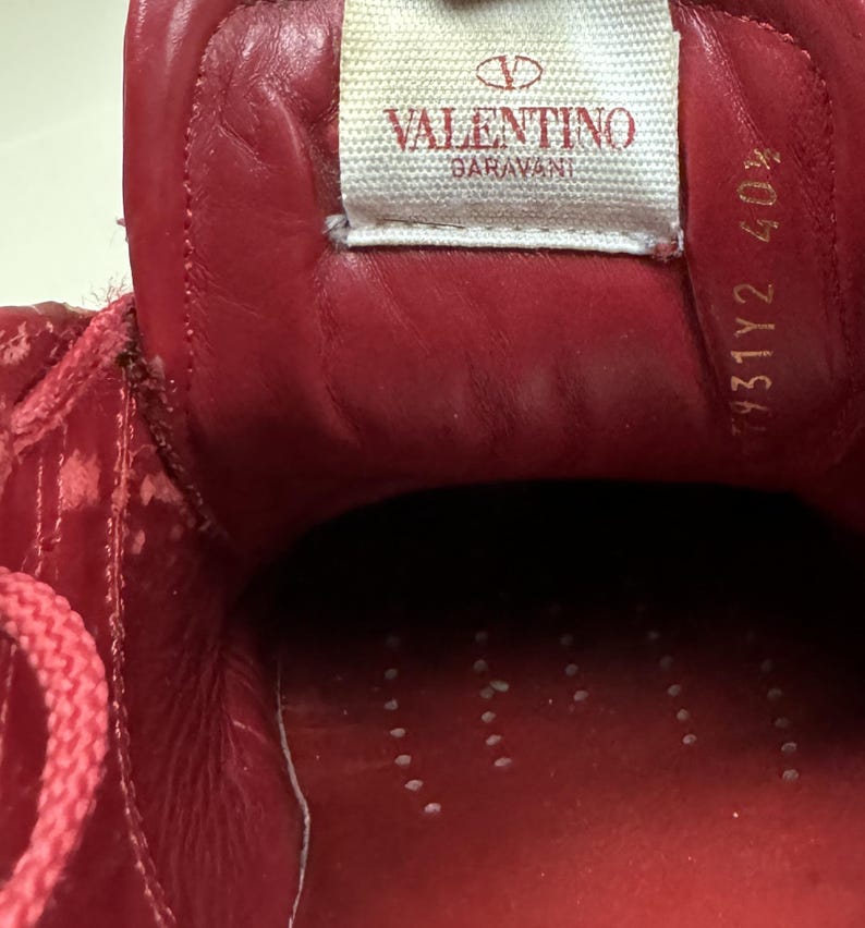May include: Red leather interior of a shoe with the Valentino Garavani logo and the size 431Y2 40% printed on the inside.