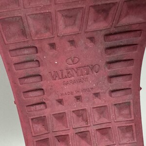 May include: Close-up of the red rubber sole of a shoe with the text "VALENTINO GARAVANI MADE IN ITALY" embossed on the sole.