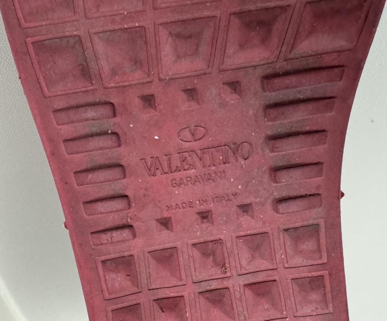 May include: Close-up of the red rubber sole of a shoe with the text "VALENTINO GARAVANI MADE IN ITALY" embossed on the sole.