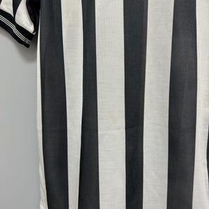 May include: Close-up of a black and white striped shirt. The shirt has vertical stripes and a white collar with black trim. The fabric appears to be a breathable material, suitable for athletic wear or casual use.