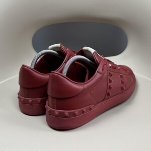 May include: A pair of red leather trainers with a white rubber sole and red studded detailing.