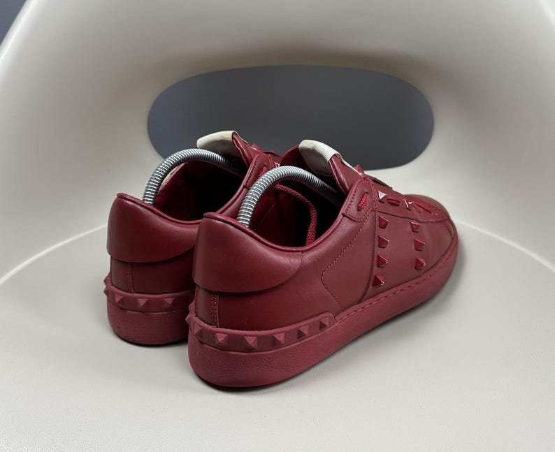 May include: A pair of red leather trainers with a white rubber sole and red studded detailing.