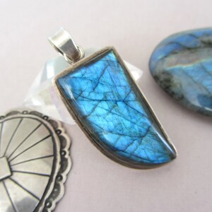 May include: A silver pendant featuring a large, iridescent blue labradorite gemstone. The stone is cut in a unique, curved shape and has a beautiful, shimmering effect.