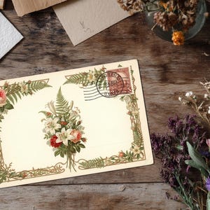 May include: Vintage postcard with floral illustrations, including roses and lilies, and a postage stamp. The postcard is cream-colored with a decorative border and a bouquet of flowers in the center. Dried flowers and paper scraps are on a wooden surface.