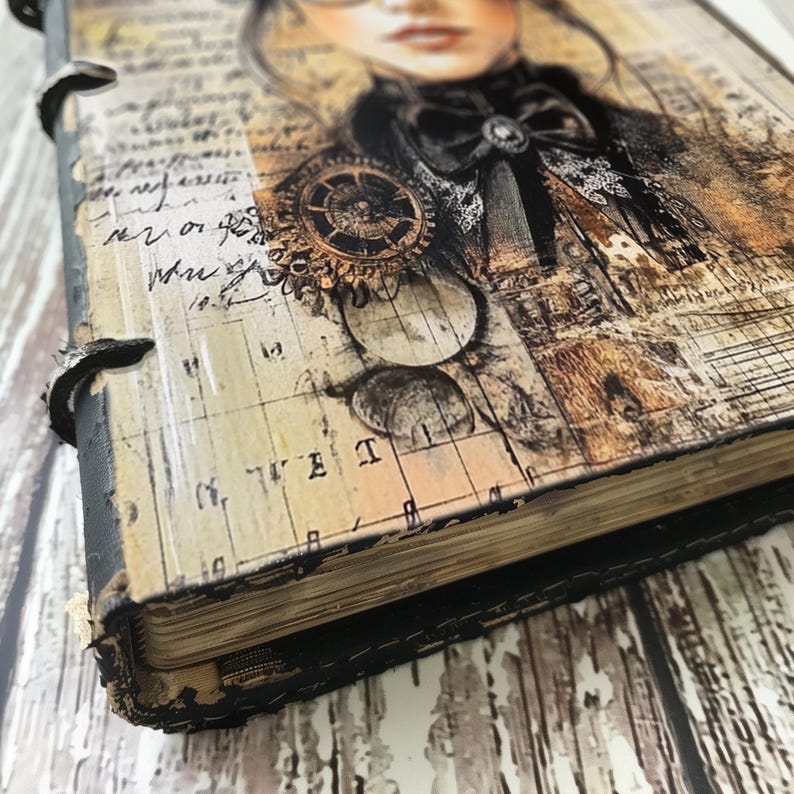 K&ouml;nnte beinhalten: Ein Vintage-Notizbuch mit schwarzem Lederbezug und einem dekorativen Design mit einer Frau mit Schleife und Zahnrad. Das Notizbuch hat einen abgenutzten Look und ist mit Metallringen gebunden.