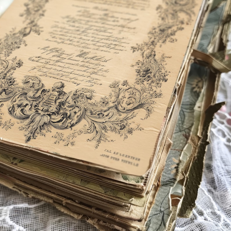May include: An antique book with aged, cream-colored pages. The pages feature ornate black floral and scrollwork designs, with handwritten text. The book's edges show signs of wear, adding to its vintage aesthetic. The book is open, revealing multiple pages.