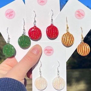 Può includere: Sei paia di orecchini pendenti con una varietà di motivi di ornamenti natalizi. Gli ornamenti sono realizzati in resina e hanno una finitura lucida. Gli ornamenti sono decorati con glitter e strisce. Gli orecchini sono di colore argento e hanno una chiusura a gancio.