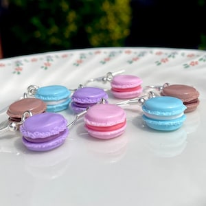 Könnte beinhalten: Sechs Paare Macaron-Ohrringe mit silbernen Haken. Die Macarons sind in verschiedenen Farben, darunter rosa, lila, blau und braun.