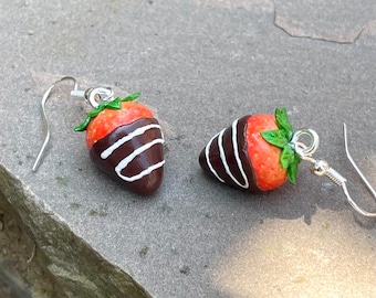 May include: A pair of silver dangle earrings featuring a red and white chocolate-covered strawberry design.