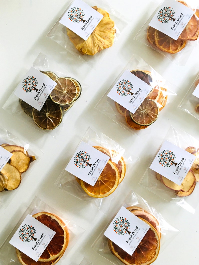 May include: Nine individual clear plastic bags containing dried fruit slices. Each bag has a white label with a small orange tree graphic and the text "Fresh Dried" with a tagline underneath. The bags contain dried pineapple, orange, lime, and apple slices.