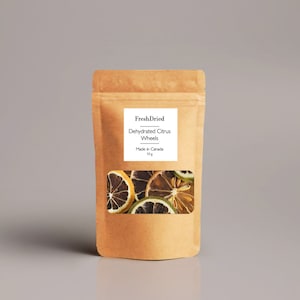 May include: A brown paper bag with a clear window showing dried citrus wheels. The bag has a white label with the text "FreshDried Dehydrated Citrus Wheels Made in Canada 10 g". The dried citrus slices are various shades of brown and yellow.