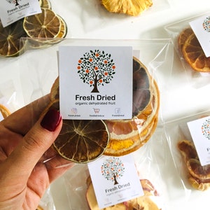 May include: Assortment of dried fruit in individual clear plastic bags. The bags contain dried pineapple, orange slices, apple slices, and lemon slices. The bags are labeled with the text "Fresh Dried" and a logo of a tree with orange fruit.