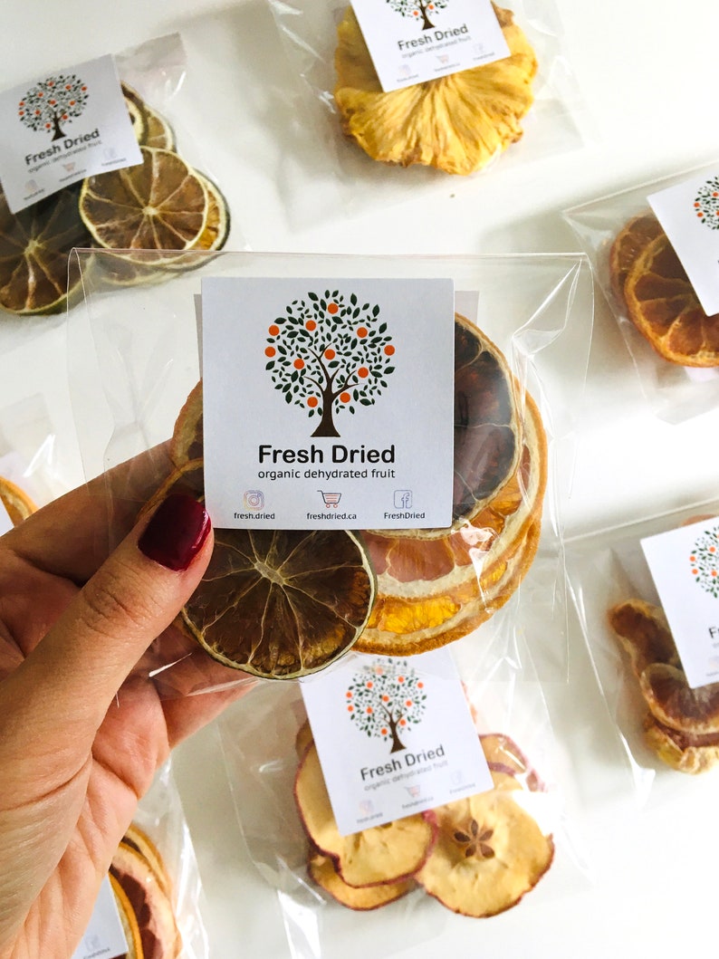 May include: Assortment of dried fruit in individual clear plastic bags. The bags contain dried pineapple, orange slices, apple slices, and lemon slices. The bags are labeled with the text "Fresh Dried" and a logo of a tree with orange fruit.