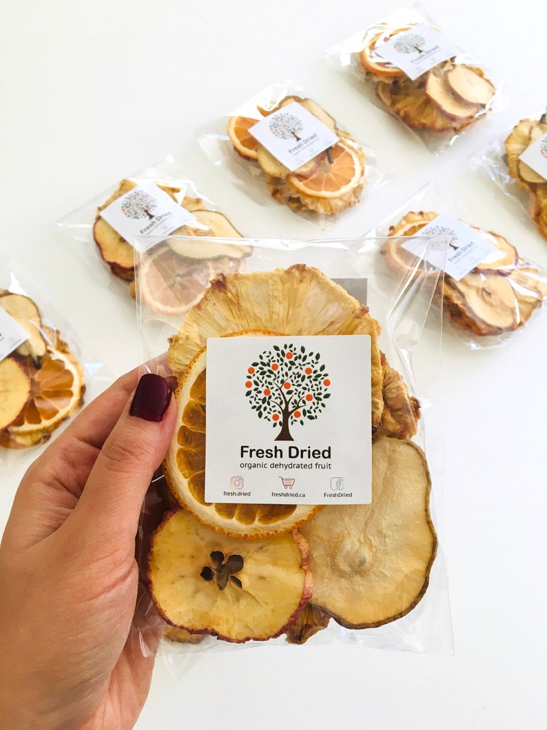 May include: A clear plastic bag filled with dried fruit slices. The fruit includes apple, pear, pineapple, and orange slices. The bag has a white label with the text "Fresh Dried organic dehydrated fruit" and social media icons.