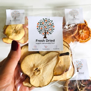 May include: A clear plastic bag filled with dried pear slices. The bag has a label that says "Fresh Dried organic dehydrated fruit" with a logo of a tree with green leaves and orange fruit. The website address "freshdried.ca" is printed on the label.