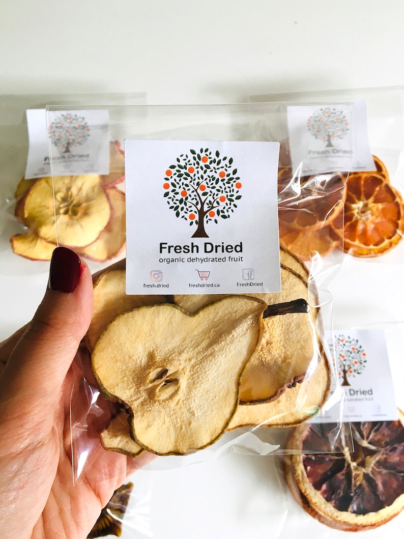 May include: A clear plastic bag filled with dried pear slices. The bag has a label that says "Fresh Dried organic dehydrated fruit" with a logo of a tree with green leaves and orange fruit. The website address "freshdried.ca" is printed on the label.