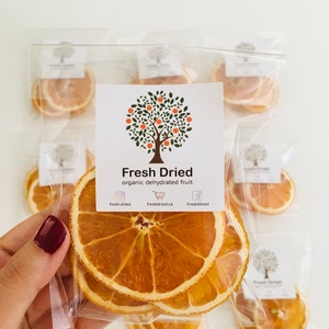 May include: A clear plastic bag filled with dried orange slices. The bag has a label that says "Fresh Dried organic dehydrated fruit" with social media icons and website information.