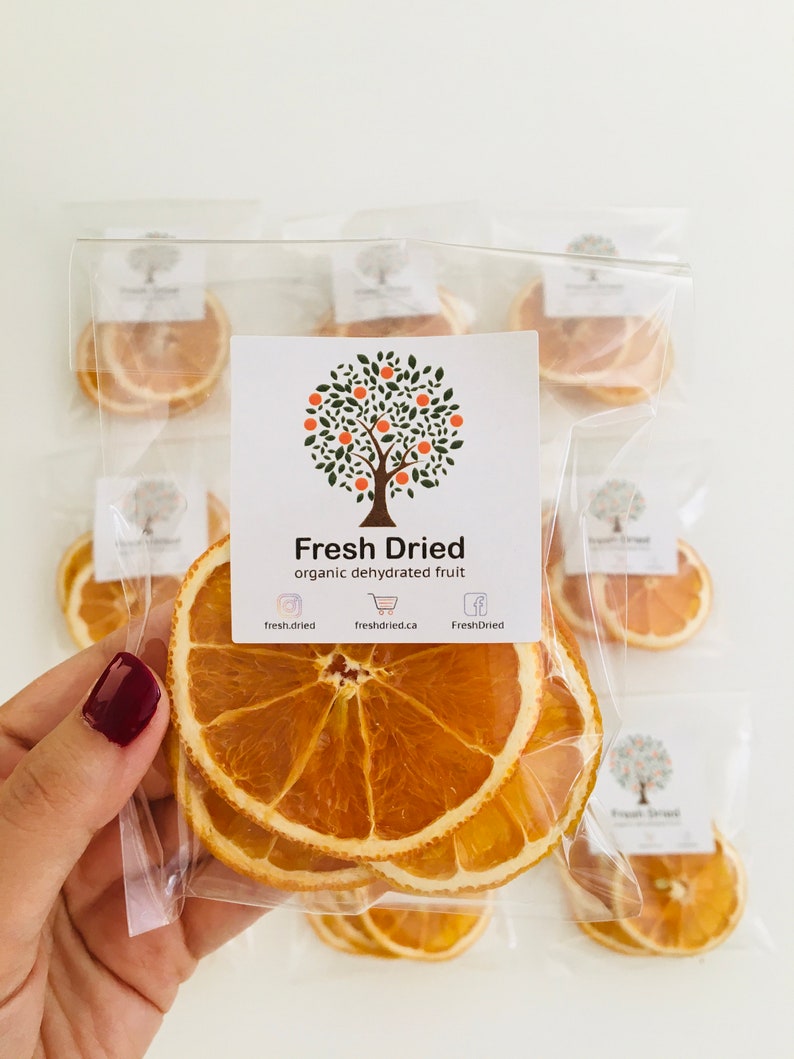 May include: A clear plastic bag filled with dried orange slices. The bag has a label that says "Fresh Dried organic dehydrated fruit" with social media icons and website information.