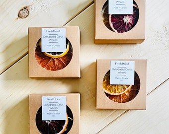 May include: Four small square boxes with brown paper packaging, each containing a stack of dehydrated citrus wheels. The boxes have a white label with the text "FreshDried Dehydrated Citrus Wheels Made in Canada 20g". The citrus wheels are in various colors, including orange, yellow, and red.