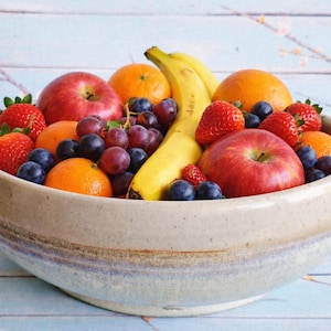 May include: A ceramic bowl overflowing with fresh fruit: red apples, oranges, strawberries, grapes, blueberries, and bananas. The bowl is beige and blue. The fruit is arranged attractively, creating a colourful and healthy display.
